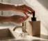 Pessoa usando porta-sabonete Rawlux Wolff em lavabo com torneira visível