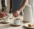 Café da tarde com xícaras Colibri, garrafa térmica branca e prato com bolo.
